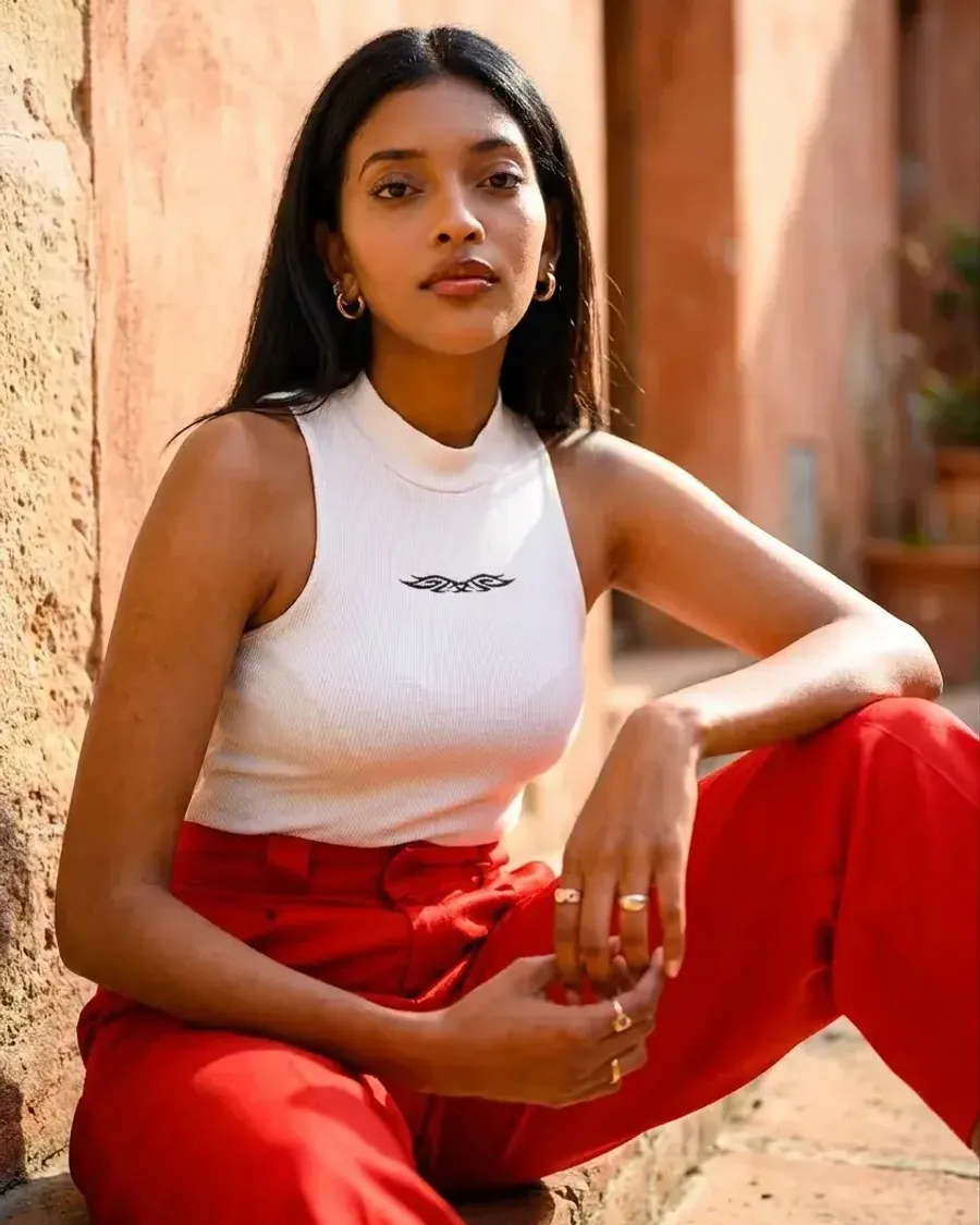A woman in a white tank and red satin trousers against a sunlit terracotta wall
