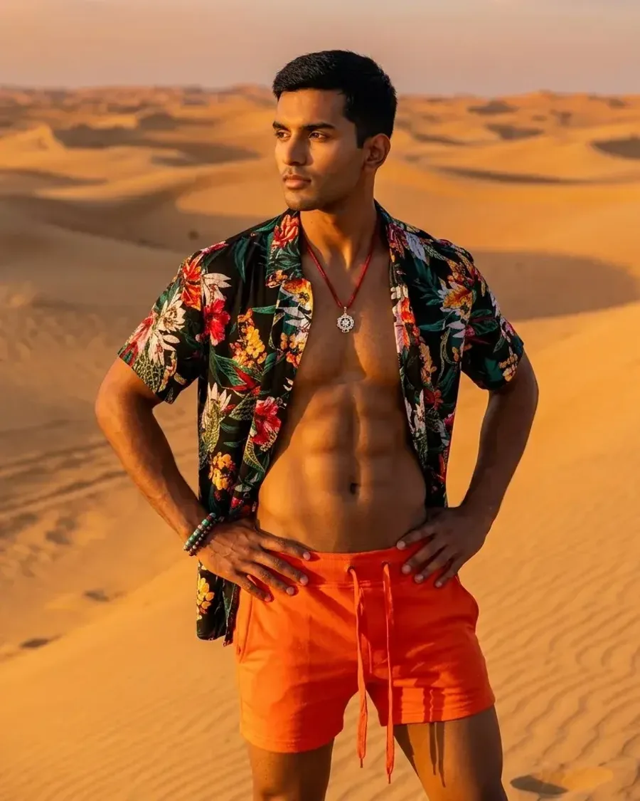 A man in an open floral shirt and orange shorts on desert dunes at golden hour