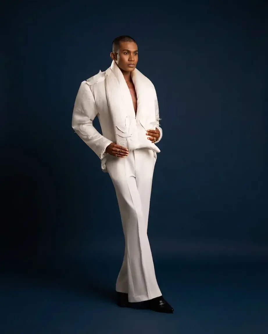 An androgynous model in a white draped avant-garde suit against a navy studio backdrop