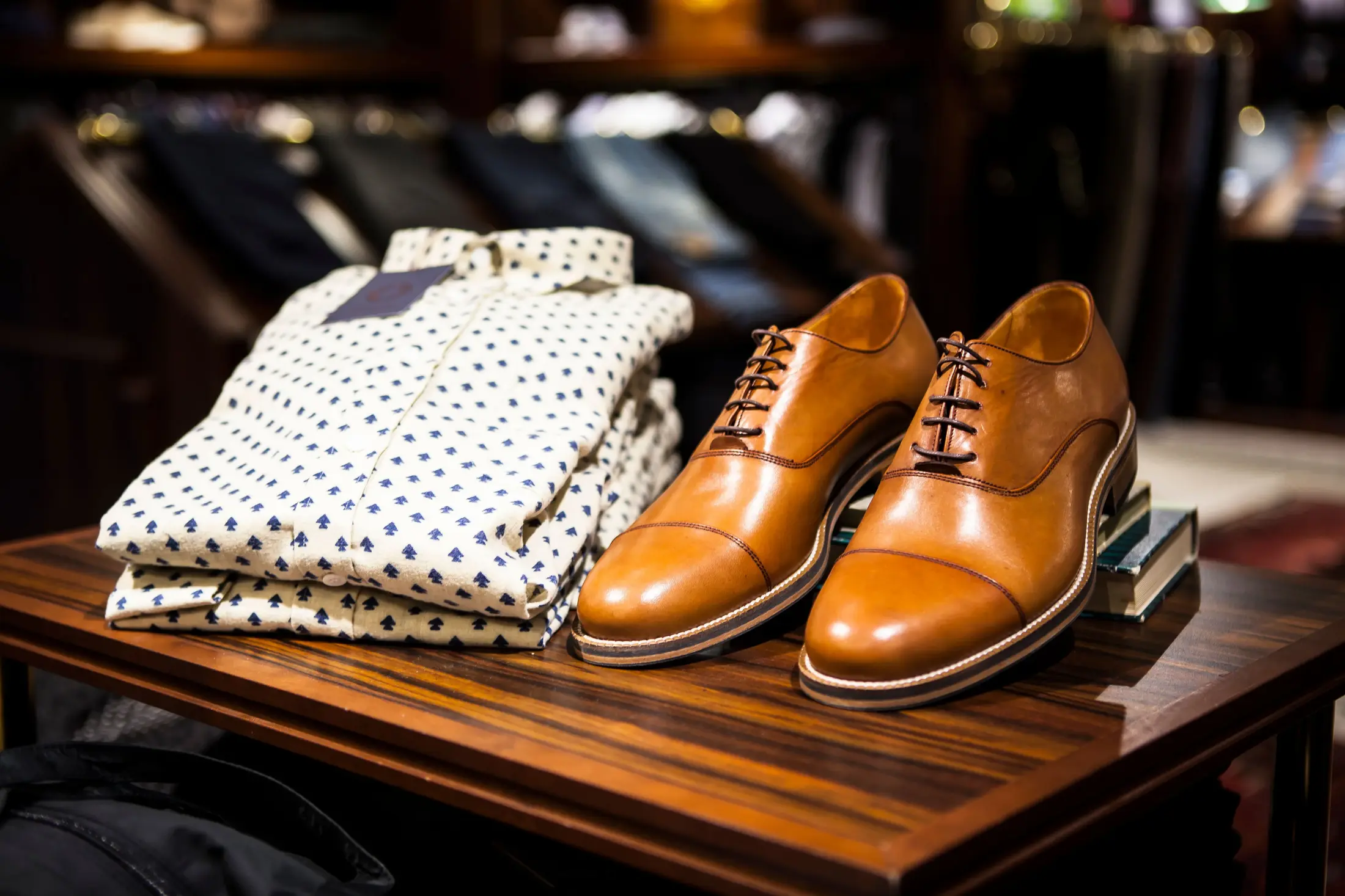 Folded shirts and leather oxford shoes laid out on a wooden table